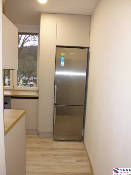 Kuchyně s podlahou s dřevěným dekorem a lednicí v 2pokojovém bytě.