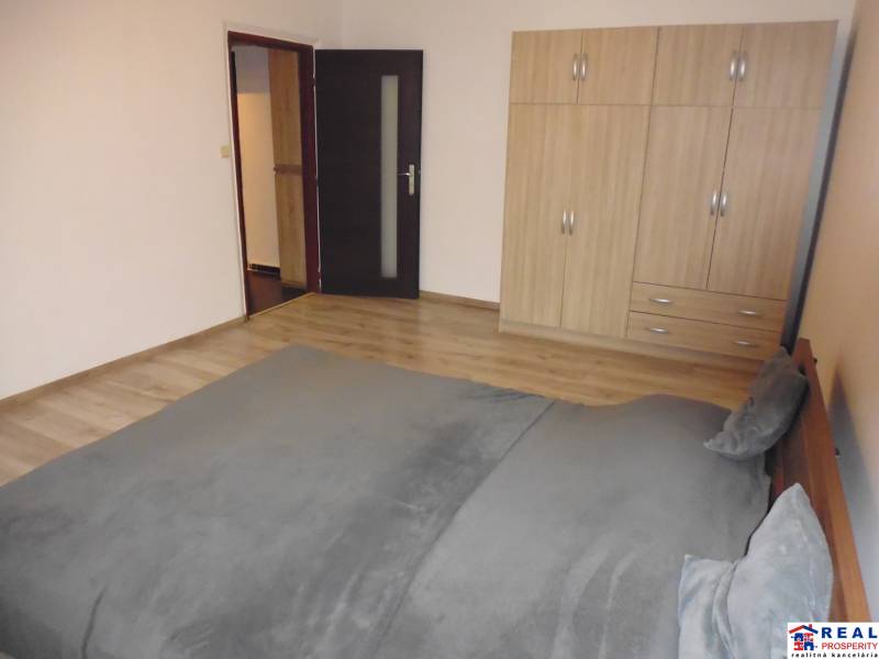 Ložnice v 2-pokojovém bytě s podlahou s dřevěným dekorem, postelí a šatní skříní.