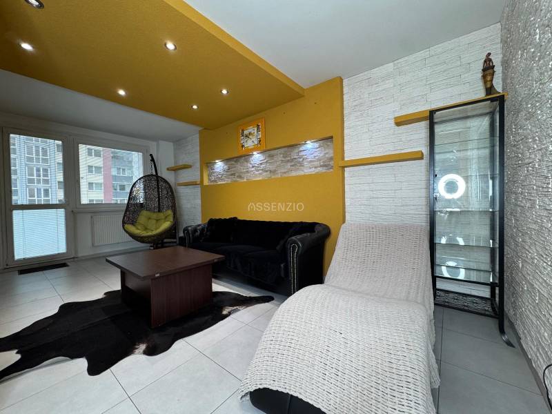 Obývací pokoj v 3-pokojovém bytě s barevnými stěnami, prosklenou vitrínou a závěsným křeslem.