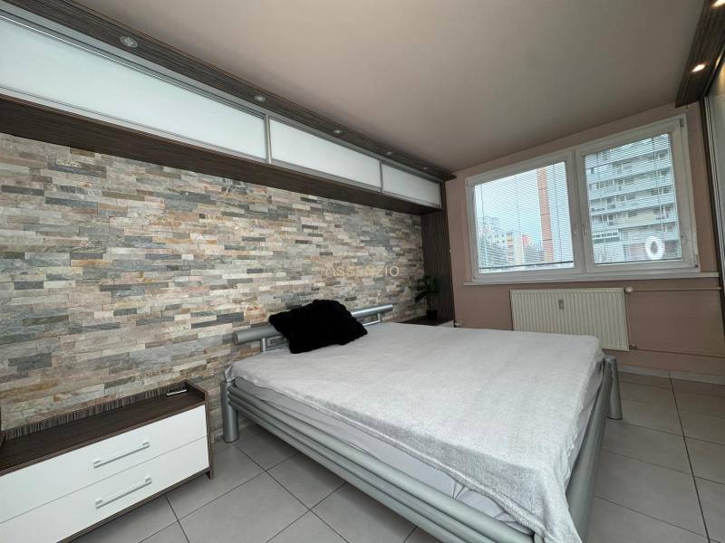 Ložnice s kamennou stěnou a velkým oknem v 3-pokojovém bytě.