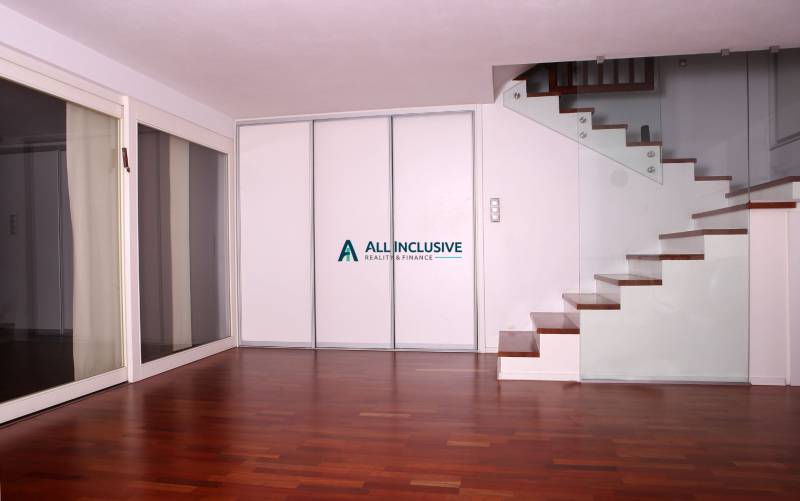 Interiér rodinného domu s podlahou s dřevěným dekorem a schodištěm se skleněným zábradlím.