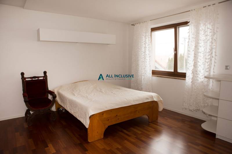 Ložnice v rodinném domě s postelí, křeslem a podlahou s dřevěným dekorem.