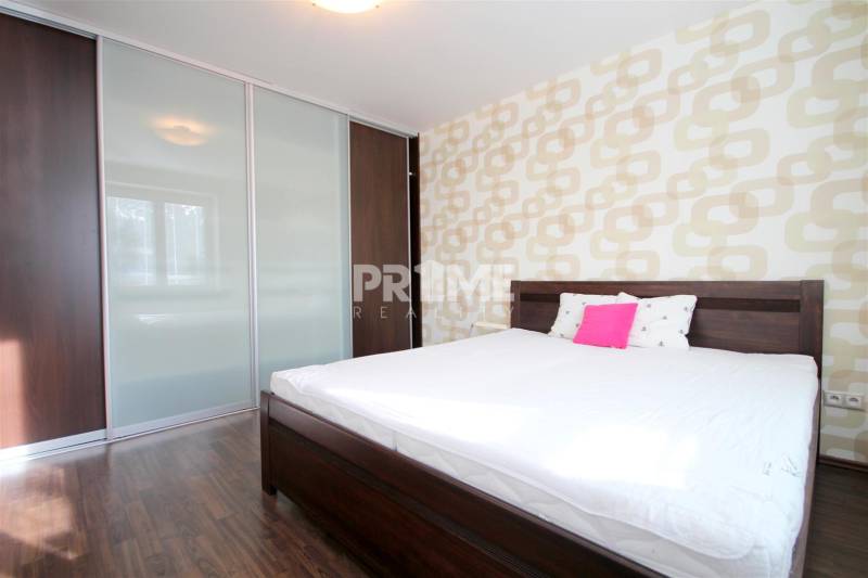 Ložnice v dvoupokojovém bytě s postelí, vestavěnou skříní a podlahou s dřevěným dekorem.