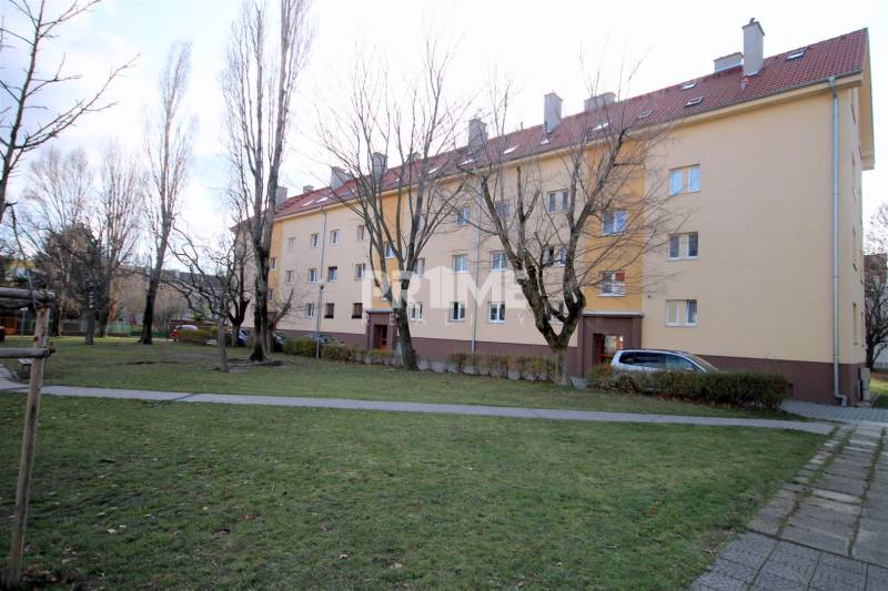 Bytový dům na Kadnárově ulici v Bratislavě - Rači obklopený zelení a chodníkem.