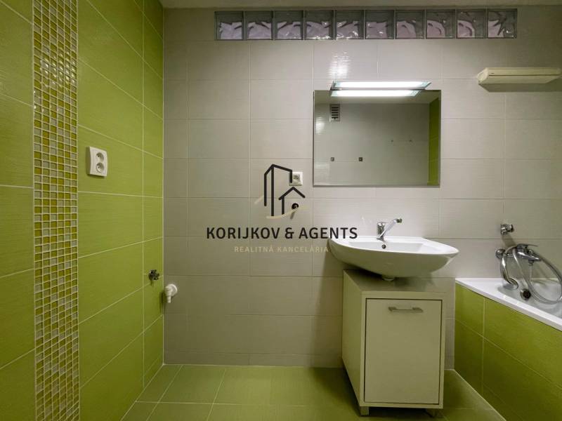 Koupelna se zelenými obklady a bílým umyvadlem v 2pokojovém bytě.