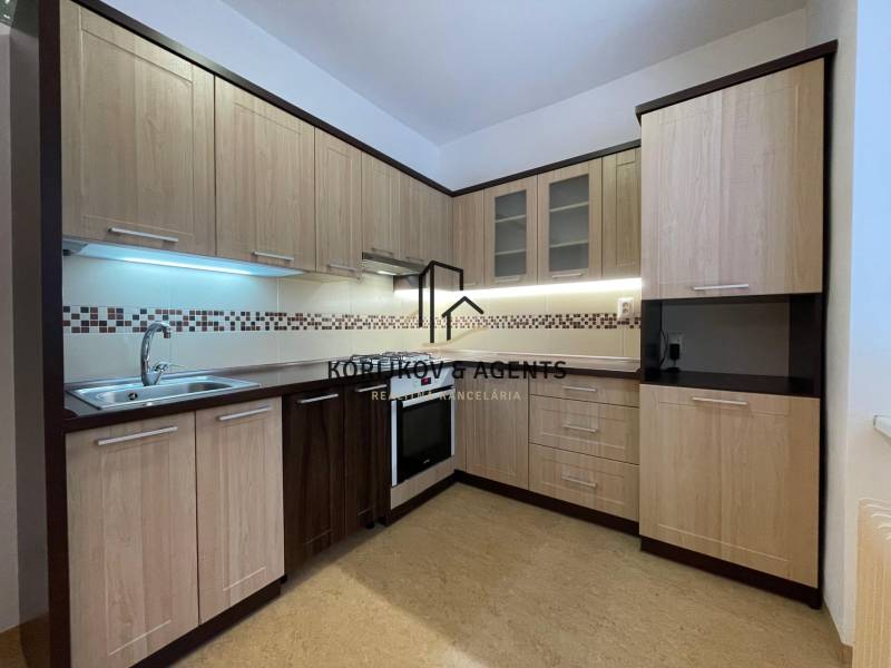 Kuchyně v 2pokojovém bytě s podlahou s dřevěným dekorem a světlým nábytkem.