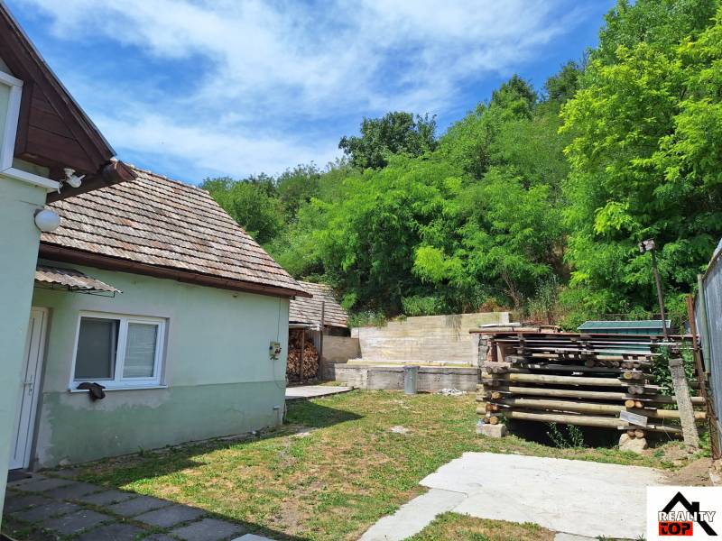 Rodinný dům v Hajnáčce s dvorem, dřevníkem a zelenými stromy v okolí.