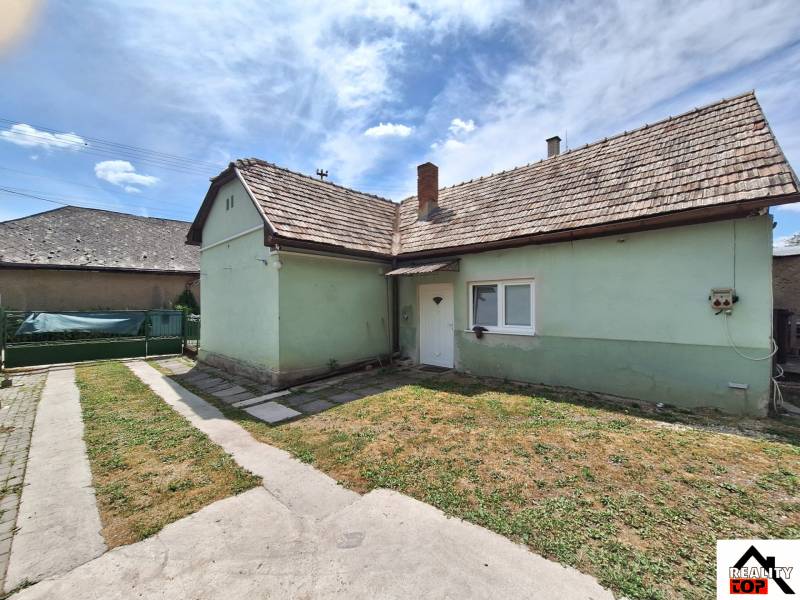 Rodinný dům v Hajnáčce s asfaltovým chodníkem a zeleným trávníkem pod modrou oblohou.