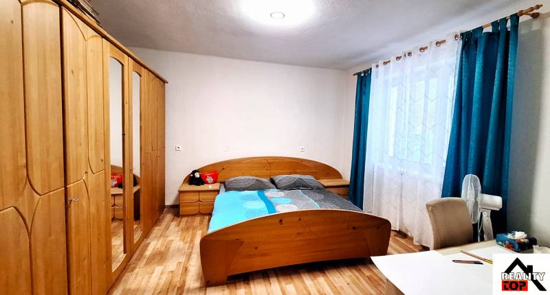 Ložnice v rodinném domě s postelí, skříní a podlahou s dřevěným dekorem.