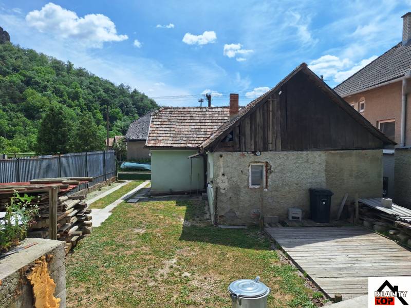 Rodinný dům v Hajnáčce s oploceným dvorem, dřevěnou přístavbou a uskladněným dřevem.