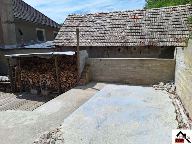 Dvůr rodinného domu v Hajnáčce s dřevníkem a betonovou plochou.
