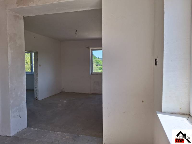 Interiér rodinného domu s nedokončenými stěnami a betonovou podlahou.