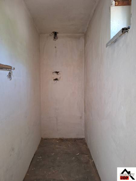 Úzký interiérový prostor v rodinném domě s malým oknem a betonovou podlahou.