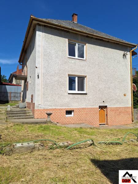 Rodinný dům v Šíde se strmou střechou a upravenou zahradou s trávníkem.