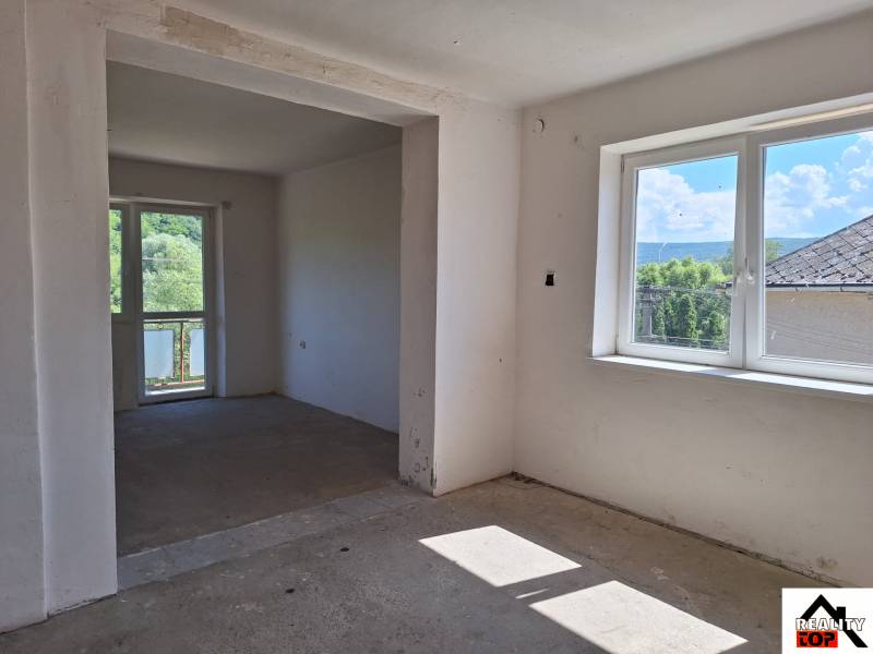 Pokoj v rodinném domě, velká okna, výhled na zahradu a okolní stromy.