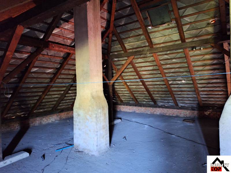 Půda rodinného domu v Šídě s dřevěnými trámy a komínem.