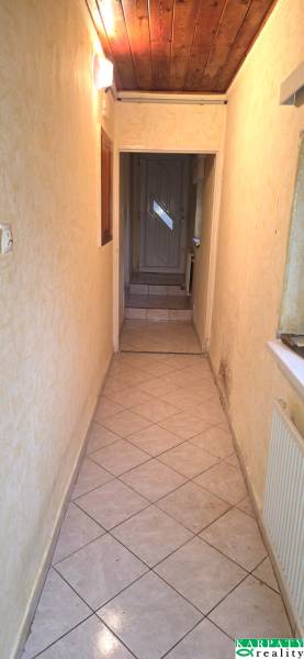 Úzká interiérová chodba s dlažbou a dřevěným stropem v rodinném domě.