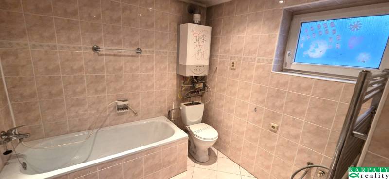 Koupelna v rodinném domě s vanou, toaletou a topením na stěně.