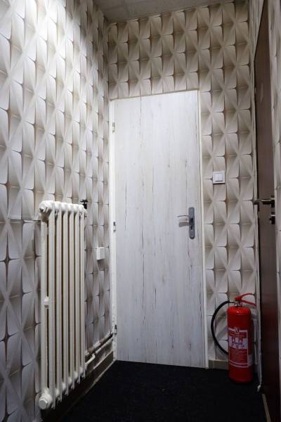 Obchodní prostory s geometrickou tapetou, dveřmi, radiátorem a hasicím přístrojem.