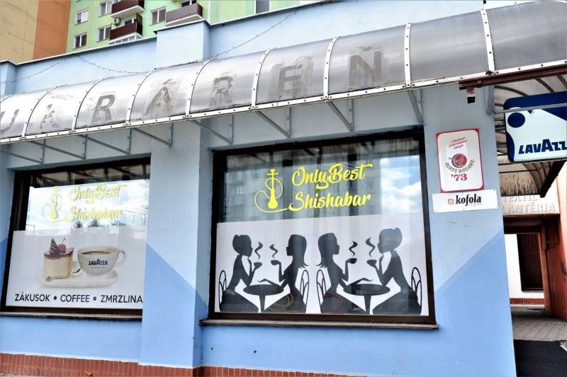 Exteriér obchodních prostor v Šali s grafickými siluetami a reklamou na kávu Lavazza.