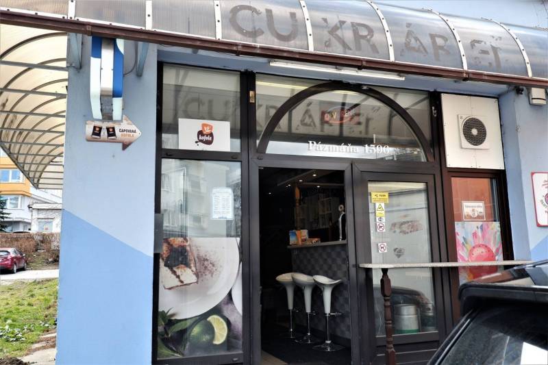 Obchodní prostory v Šali s velkým oknem, dřevěným dekorem a bílými židlemi.