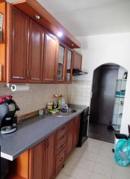 Kuchyně ve 3-pokojovém bytě s dřevěnými skříňkami a kachličkovou stěnou nad pracovní deskou.