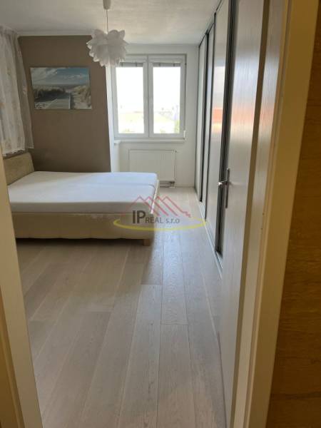 Ložnice se světlým nábytkem, velkým oknem a podlahou s dřevěným dekorem ve 4pokojovém bytě.