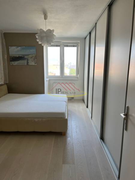 Ložnice ve 4pokojovém bytě s postelí, vestavěnou skříní a podlahou s dřevěným dekorem.