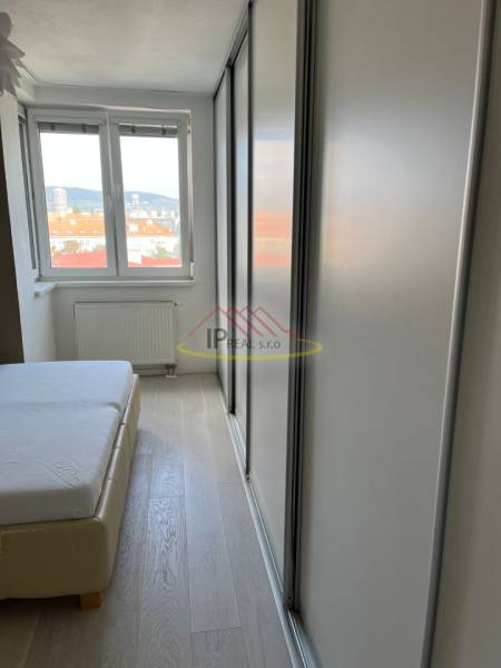 Ložnice ve 4pokojovém bytě s postelí, podlahou s dřevěným dekorem a skříní.