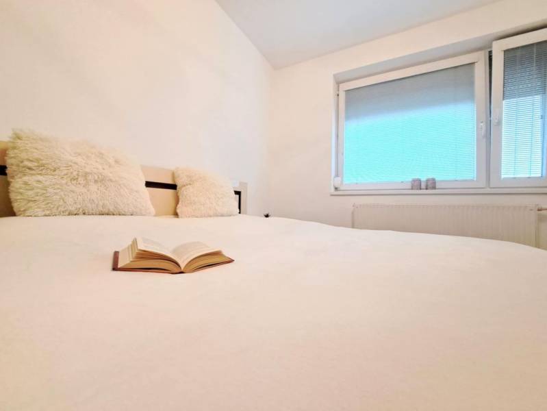 Pohled na postel s otevřenou knihou a oknem v 2-pokojovém bytě.