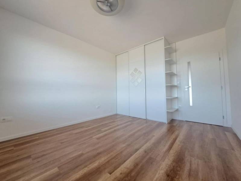 Pokoj v 2-pokojovém bytě s podlahou s dřevěným dekorem, bílou skříní a policemi.