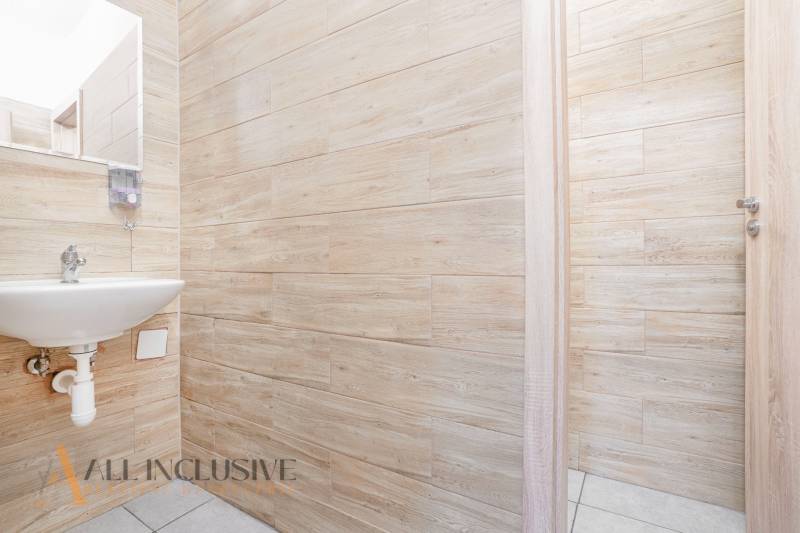 Interiér kanceláře s umyvadlem, dřevěnými stěnami a otevřenými dveřmi.