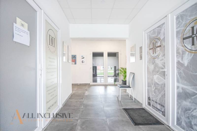 Světlý interiér s dveřmi do obchodních prostor na ulici Vajanského s přítomností rostlin.