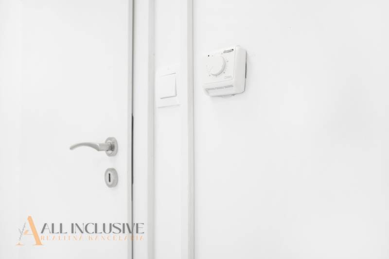 Bílá stěna s termostatem a klikou v kanceláři.