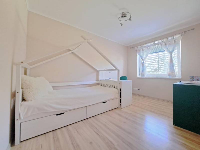 Dětský pokoj v rodinném domě s postelí ve tvaru domečku a podlahou s dřevěným dekorem.