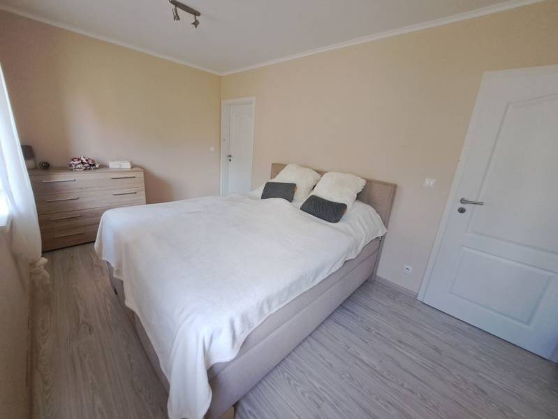 Ložnice v rodinném domě s postelí, komodou a podlahou s dřevěným dekorem.