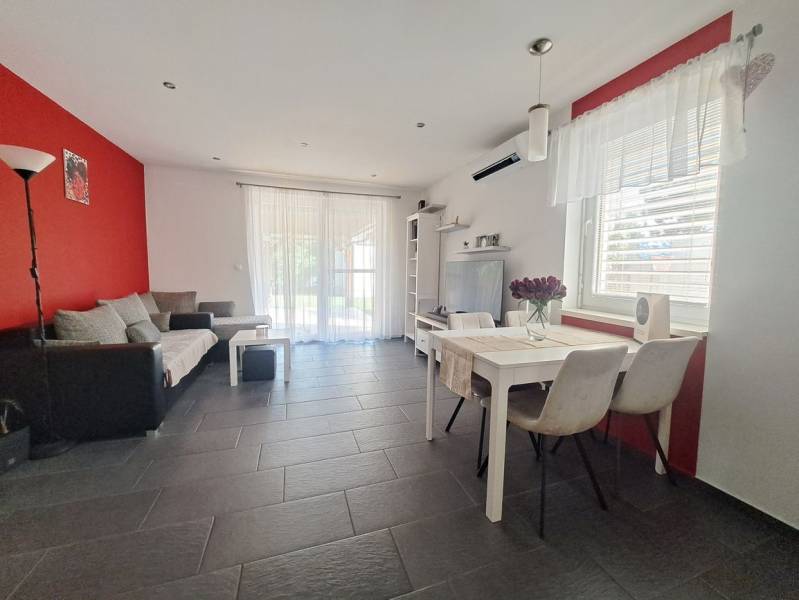 Obývací pokoj v rodinném domě s červenou stěnou, šedou dlažbou a bílým nábytkem.