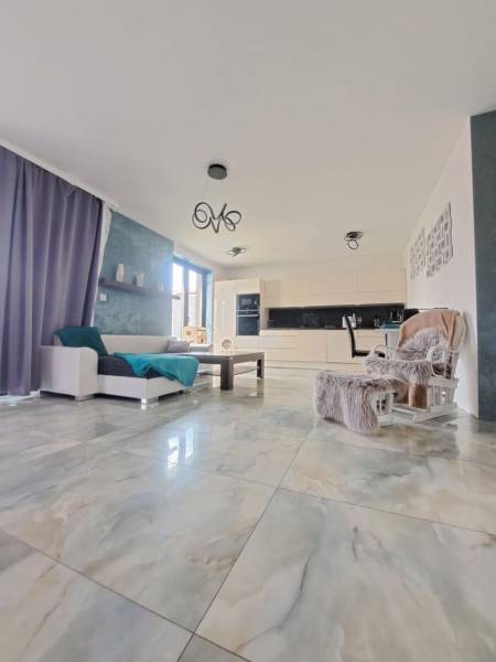 Obývací pokoj s velkými okny a světlými dlaždicemi v rodinném domě.