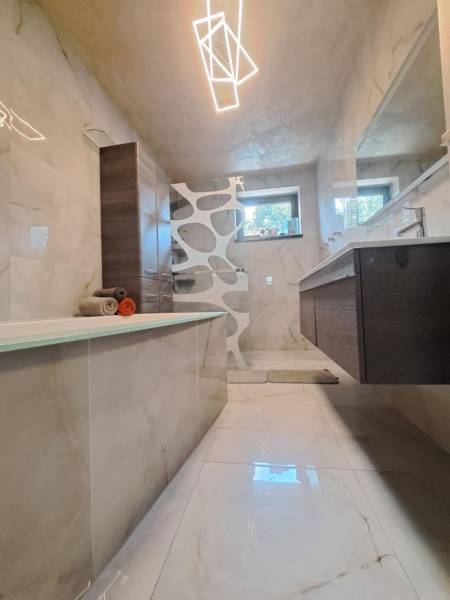 Koupelna v rodinném domě s vanou, moderním osvětlením, dlažbou a umyvadlem.