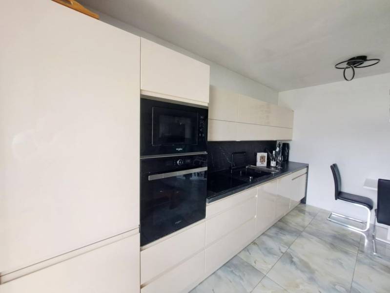 Kuchyně v rodinném domě s lesklou linkou a vestavěnými spotřebiči, podlaha s mramorovým vzorem.