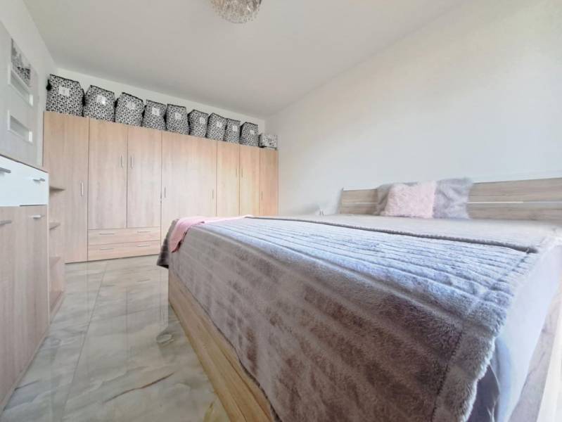 Ložnice v rodinném domě s manželskou postelí, skříní a podlahou s dřevěným dekorem.