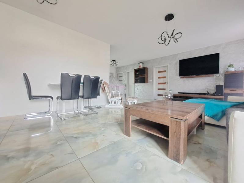 Interiér rodinného domu se světlými dlaždicemi, moderním nábytkem a stěnou s televizorem.