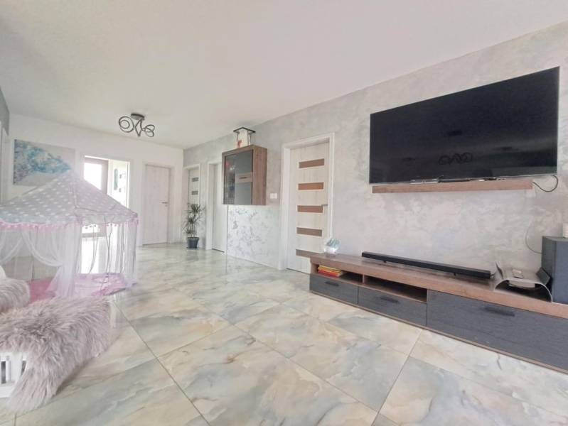 Obývací pokoj v rodinném domě s televizí na stěně, stanem a keramickou podlahou.