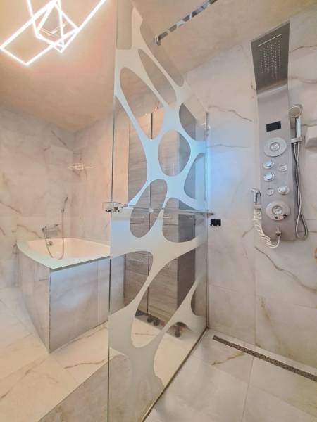 Koupelna s moderním sprchovým koutem, vanou a designovým osvětlením v rodinném domě.