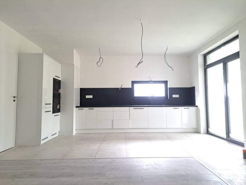 Kuchyně v rodinném domě s podlahou s dřevěným dekorem, bílými skříňkami a vestavěnými spotřebiči.