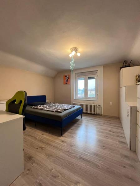 Ložnice v rodinném domě s podlahou s dřevěným dekorem, postelí a pracovním stolem.