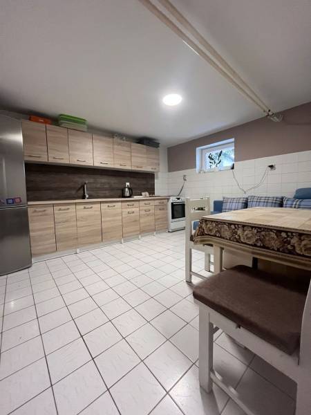 Kuchyně v rodinném domě s dlažbou, dřevěnými skříňkami, lednicí a jídelním stolem.