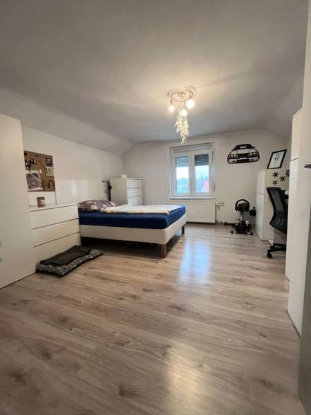 Ložnice v rodinném domě s postelí, bílým nábytkem a podlahou s dřevěným dekorem.