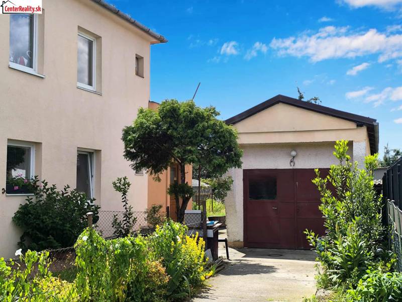 Rodinný dům v Partizánskem s garáží obklopený zahradou plnou zelených rostlin.