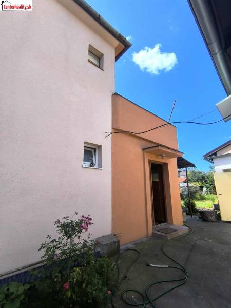 Rodinný dům v Partizánském s dvorem, květinami a hadicí na betonovém chodníku.